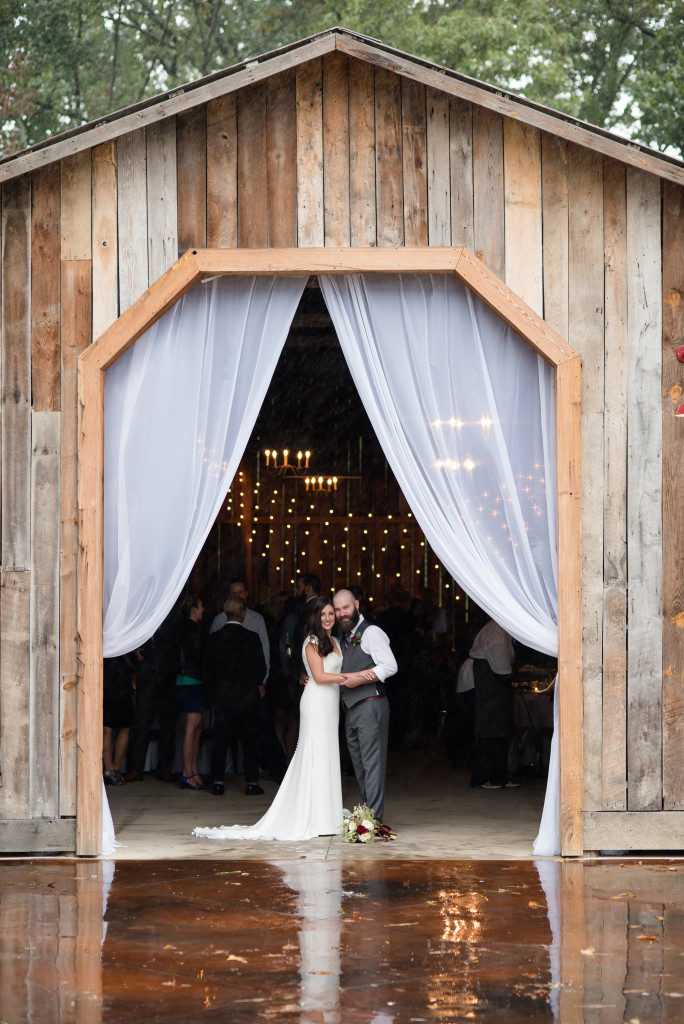 Wedding couple standing in front of their wedding string lighting at the entrance to a barn