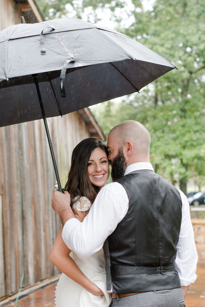 Wedding couple smiling and cuddling under an umbrella on a rainy wedding day