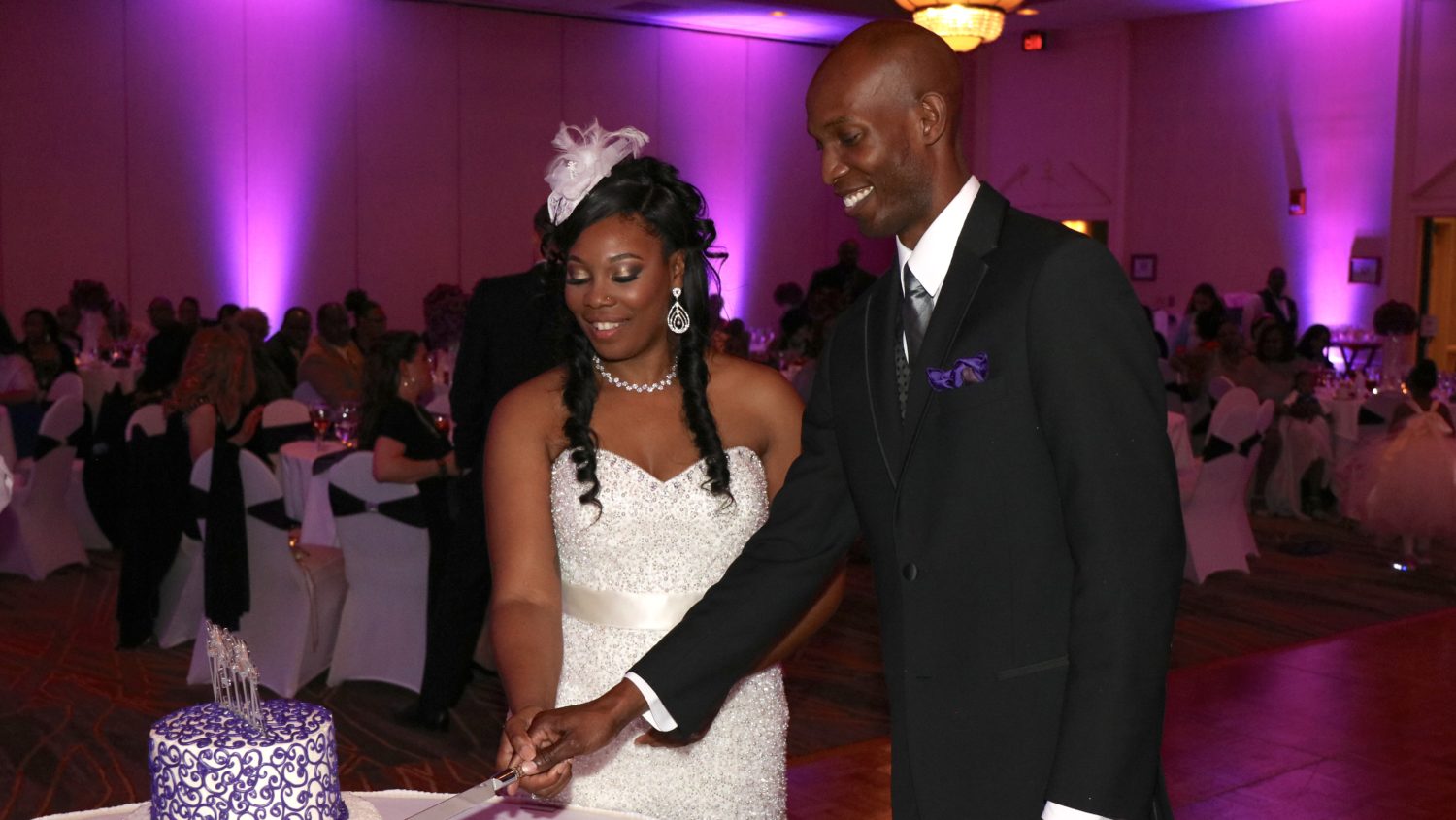 bride and groom cutting cake with purple uplights