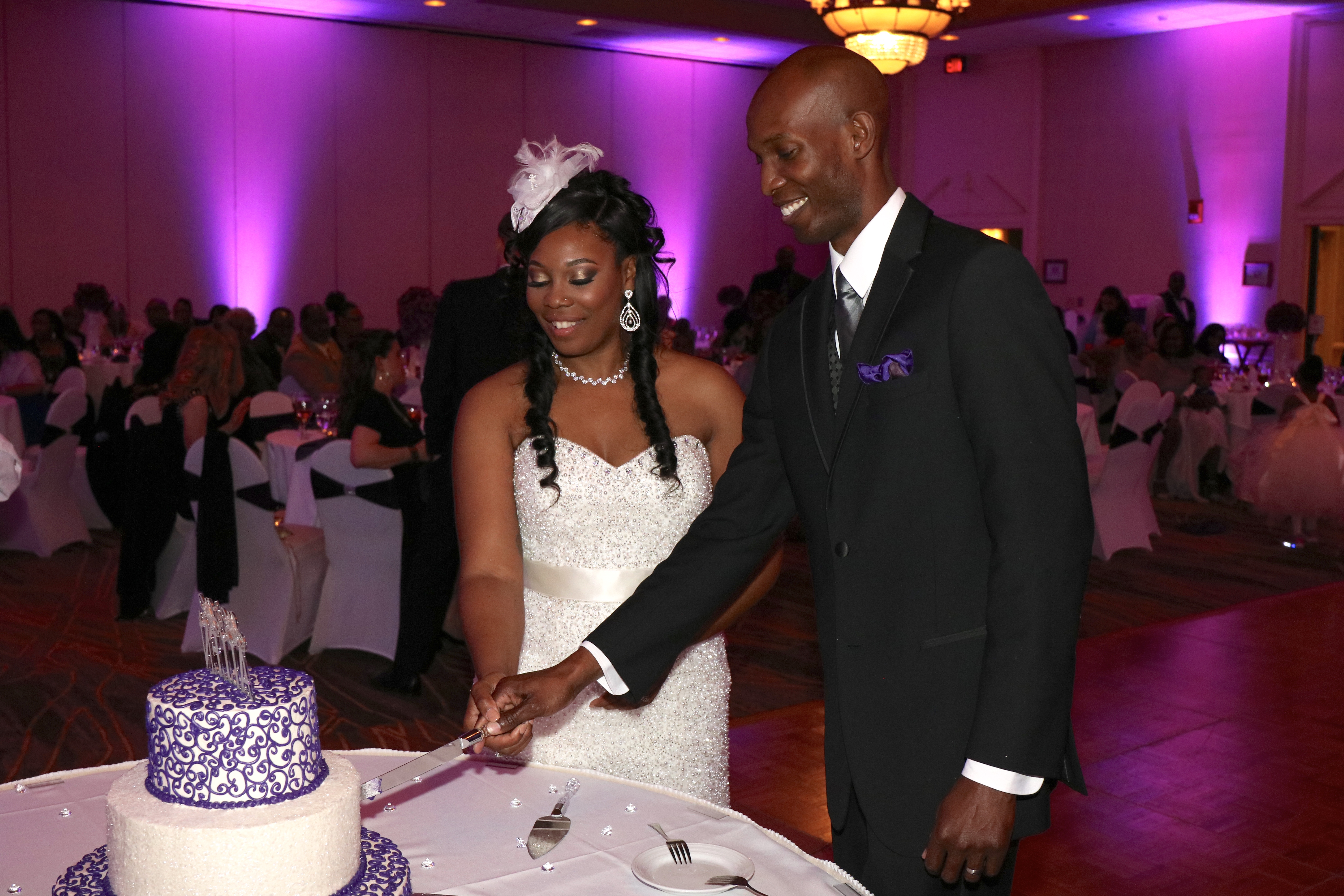 Wedding couple cutting cake with purple wedding lighting behind them