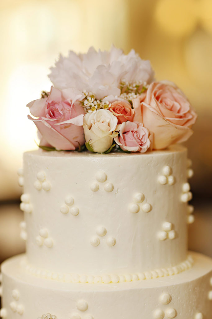 top tier of wedding cake covered in white and pink flowers at romantic pinehurst wedding