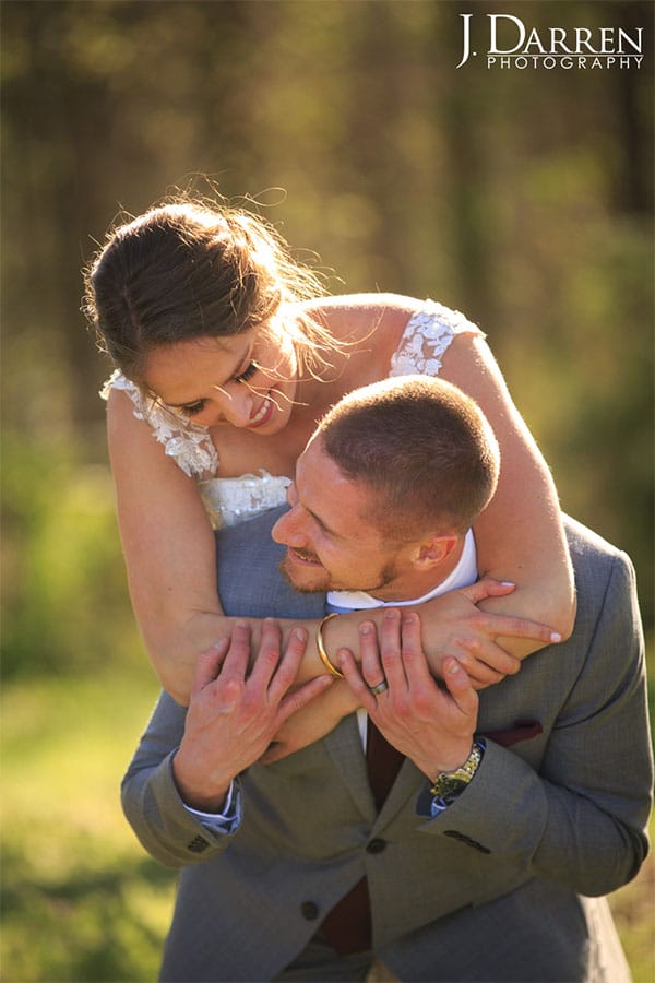 The bride is on the grooms back with greenery in the background.