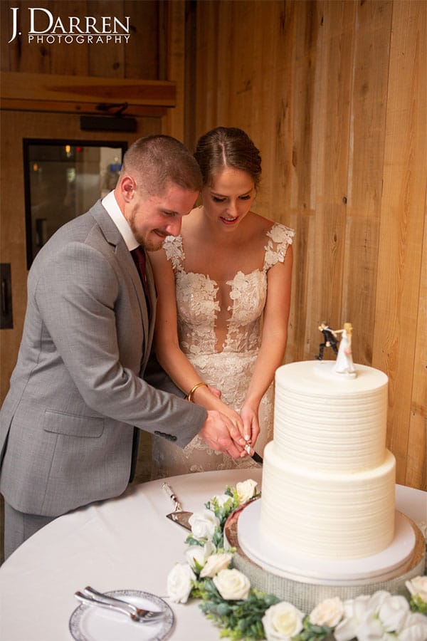 The bride and groom are cutting their wedding cate together. 