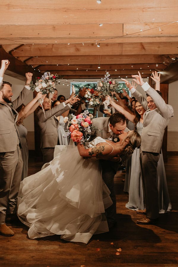 The bride and groom kissing with their friends and family in the back. 