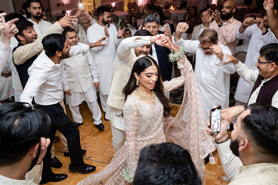 Bride and groom dancing together. Their friend's and family are dancing in the background.