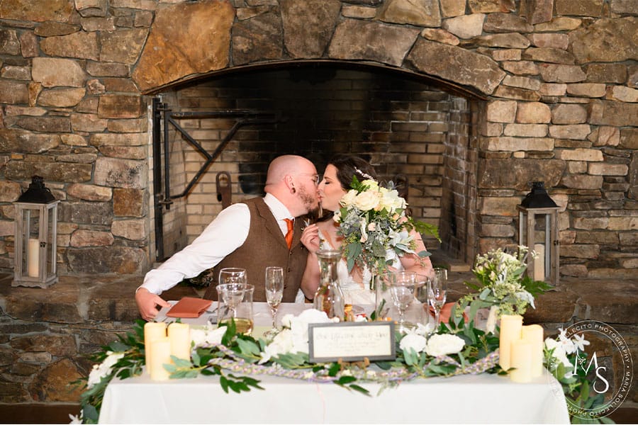 The bride and groom kissing with beautiful floral pieces in front of them.