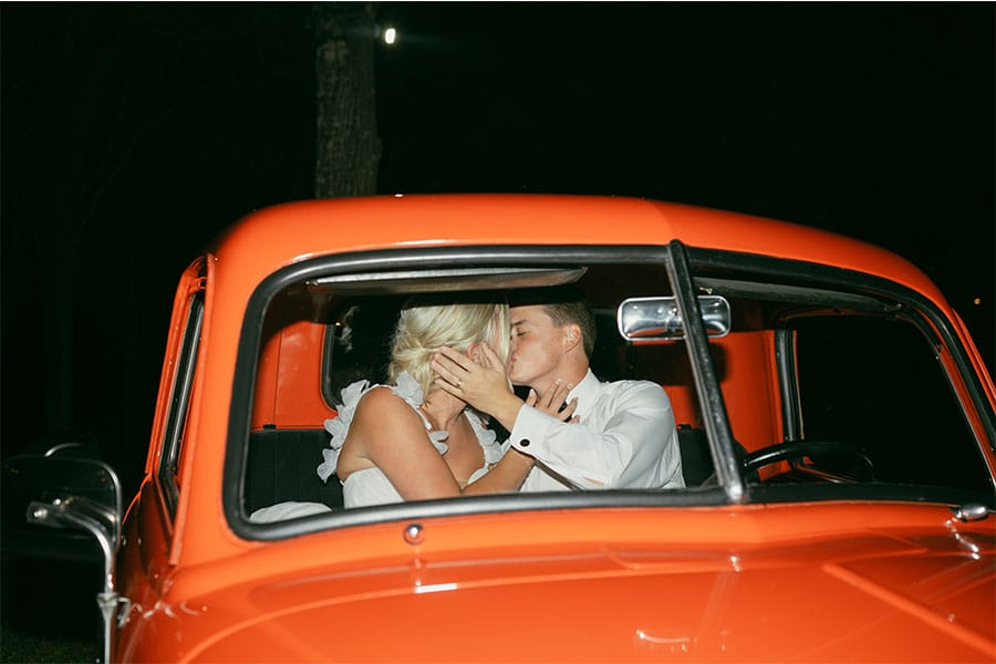 The bride and groom kissing in a red truck. 