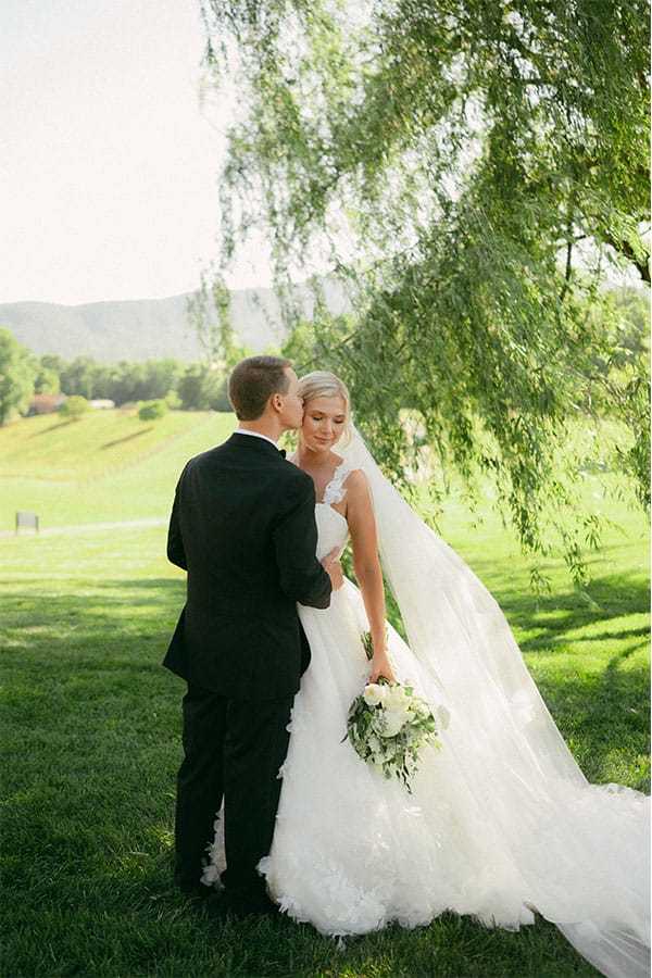 The bride and groom standing under a willow tree. 