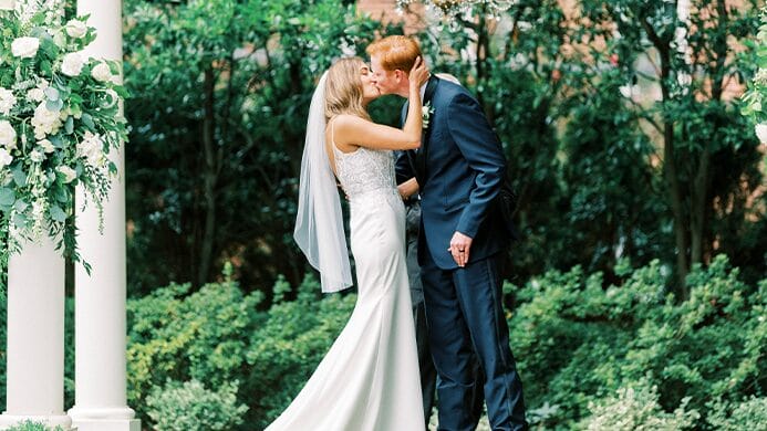 The bride and groom kissing in front of greenery.