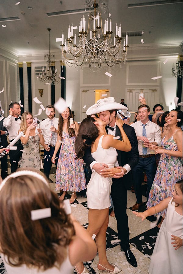 The bride and groom kissing with friends and family cheering them on.