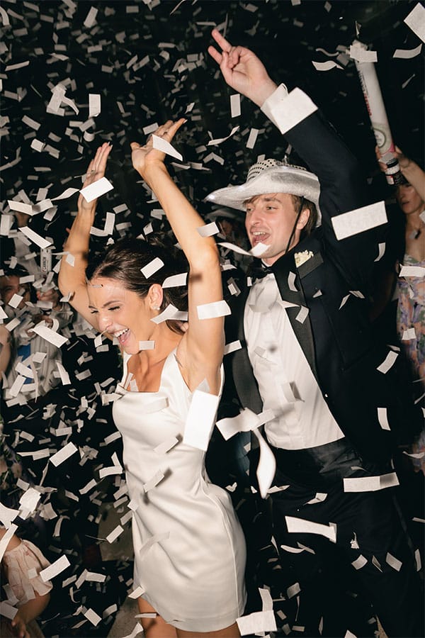 The bride and groom smiling with confetti around them.