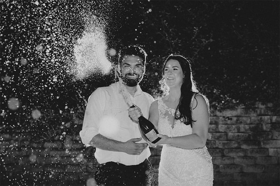 The bride and groom opening a wine bottle. 