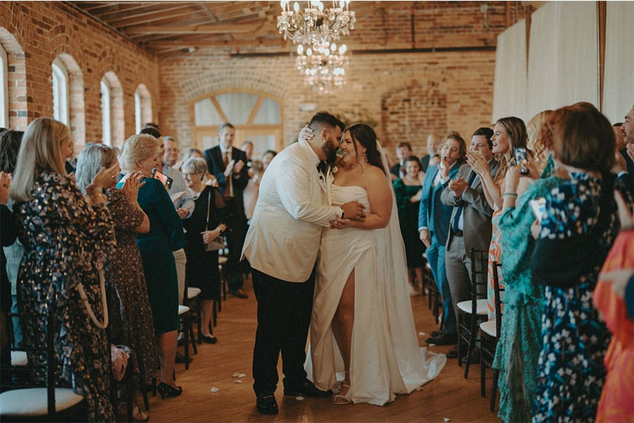 The bride and groom kissing with their loved ones around them. 