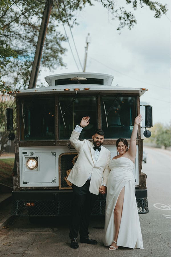 The bride and groom standing in front of a bus.