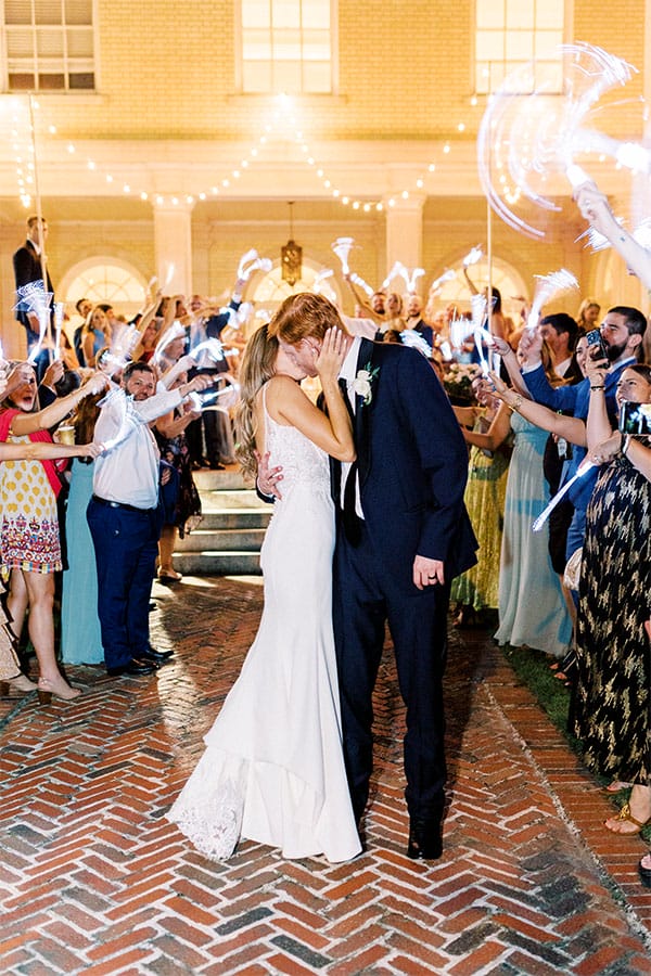 The bride and groom kissing while their loved once wave lights around. 