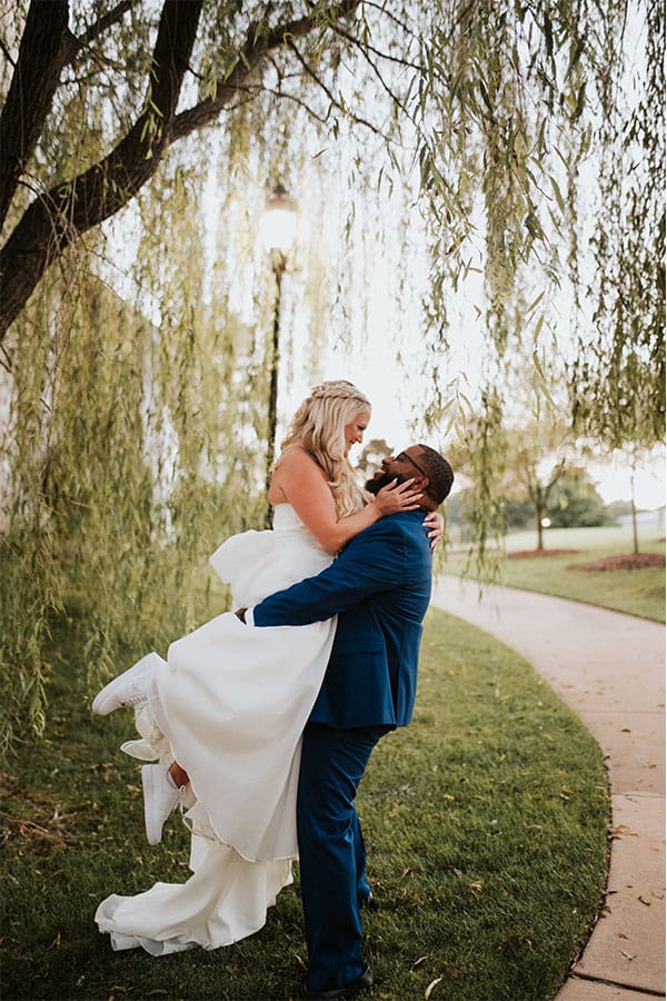 The groom holding the bride under a stunning willow tree.